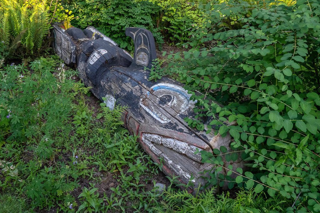 A older, faded totem pole sits among plants at Heronswood Garden