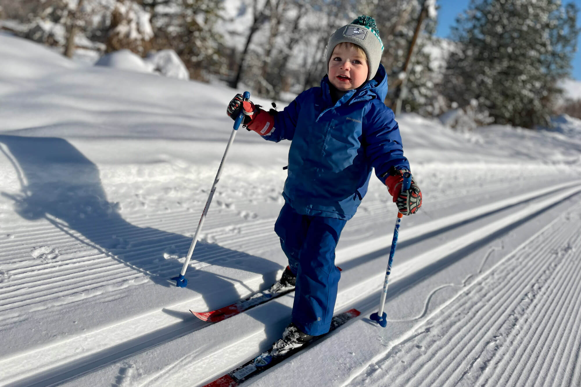 A small child in winter gear cross-country skis on flat ground