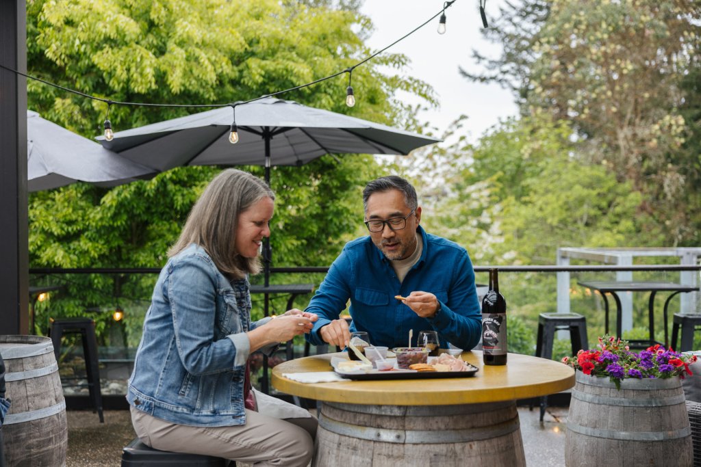 A man and woman sit at a table on a rooftop patio eating charcuterie and drinking wine on Bainbridge Island.