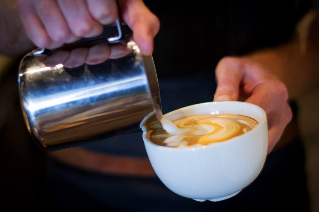 A person creates latte art at Mela Coffee Roasting Company