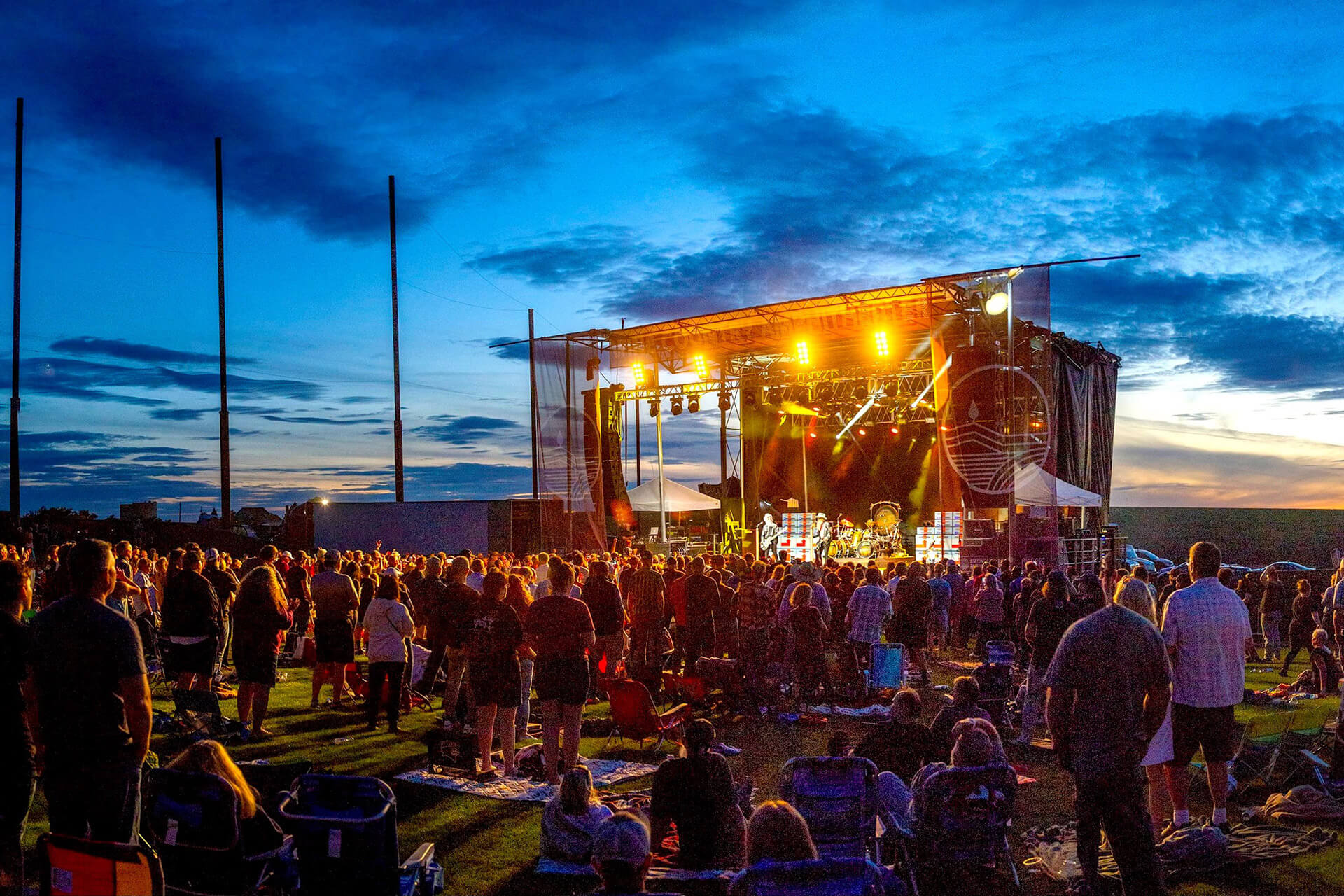 A photo of people standing and sitting on a lawn at sunset as they watch an outdoor concert at Concert Venues in Washington State